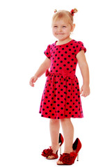 Funny little girl in a red polka dot dress trying on mommy's sho