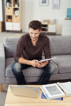 junger mann sitzt auf dem sofa und schaut auf laptop