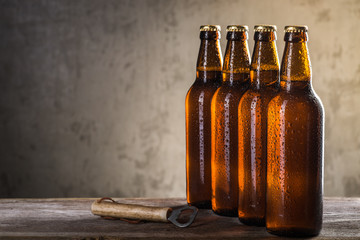 Freshly brewed beer bottles in a row with opener over the grey concrete wall