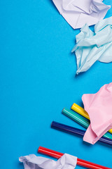 Several color pencils with crumpled color paper over the blue background