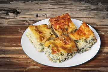 Plate of Freshly baked Serbian Traditional Zeljanica Spinach-cheese Pie slices, set on very old, weathered, cracked, scratched, peeled off, Wooden Table surface.