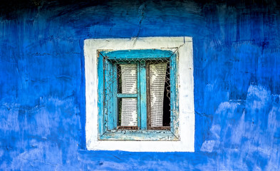 Old window with cyan wooden frame  and crocheted curtain on a blue plastered hand painted wall.