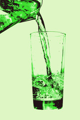 Jug pouring to glass on green background.