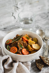 beef goulash with carrots and roasted potatoes in a white bowl on a light wooden background