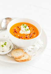 pumpkin soup with cream and paprika in a white bowl on a light wooden background