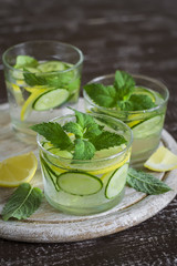 Lemonade with cucumber, lemon, mint and ginger in glass cups on a wooden surface