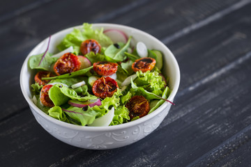 salad with fresh vegetables, garden herbs and sun-dried tomatoes in a white bowl on a dark wooden background