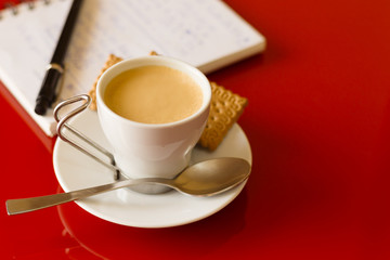 Coffee cup with cookies and a black pen over a open notebook
