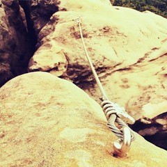 Detail of steel bolt anchor eye and rope end anchored into sandstone rock. Iron twisted rope fixed...