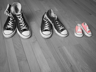 An image of two pairs of adults sneakers in black and white next to a baby pair of sneakers in pink - 86294828