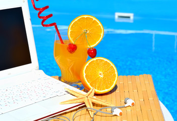 Cocktai with fruits, laptop and starfish on pool