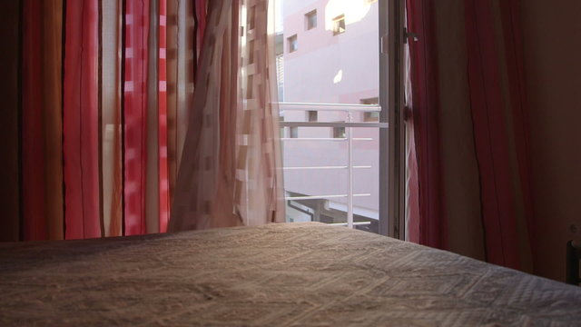 Open glass door window with waving curtains in bedroom of the hotel