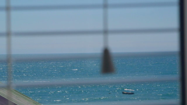 Looking out through the open window blinds at sea with floating boat