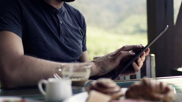 Man hands using tablet computer during breakfast on terrace
