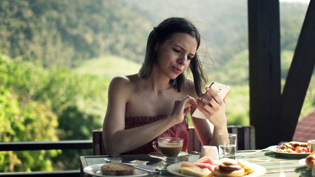 Young woman with smartphone drinking coffee on terrace
