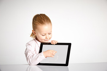Cute little and smiling girl plays with a tablet