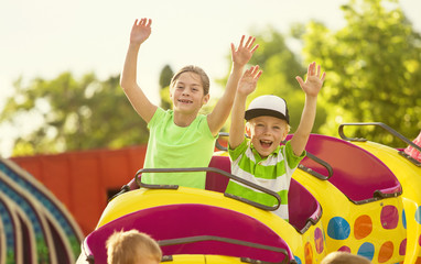 Junge und Mädchen auf einer aufregenden Achterbahnfahrt in einem Vergnügungspark mit erhobenen Armen und schreien vor Aufregung