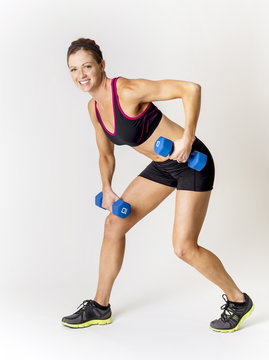 Full length photo of a beautiful, smiling fitness woman lifting weights during a workout. Indoor on a white background