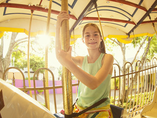 Cute smiling little girl riding on a Carnival Carousel at an amusement park or theme park. Warm...