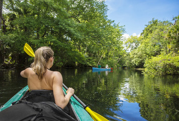 Woman kayaker paddling down a beautiful jungle river with two people in a canoe on a gorgeous day. Lots of copy space and view from behind © Brocreative