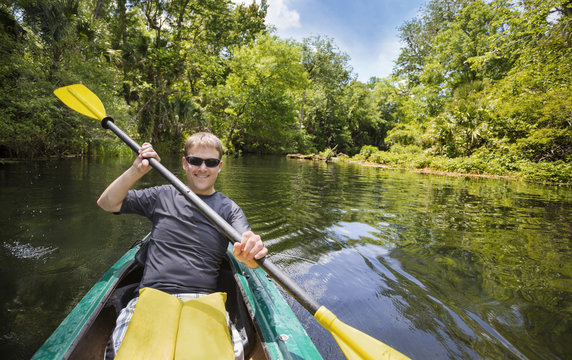 Smiling, Happy Man Kayaking Along A Beautiful Jungle River. Lots Of Copy Space In An Active Outdoor Lifestyle Photo