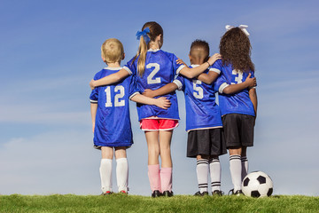Diverse group of boys and girls soccer players standing together with a ball against a simple blue sky background - Powered by Adobe