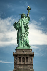 Statue of liberty seen from the back with a cloudy sky as background