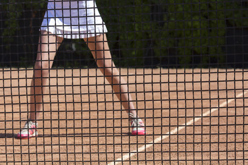 Slim legs of female tennis athlete behind fishnet barrier.
Young woman stays in ready position close to tennis playground barrier ready to return the ball white dress miniskirt focus on net