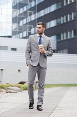 young serious businessman with paper cup outdoors