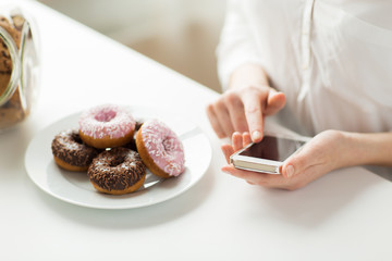 close up of hands with smart phone and donuts