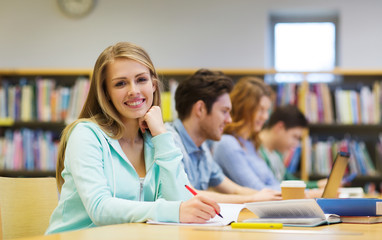 happy student girl writing to notebook in library