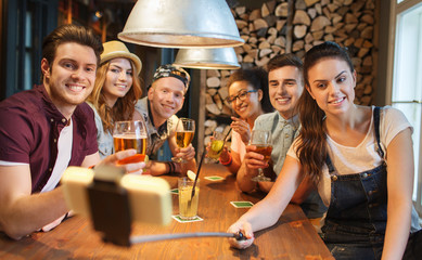 friends with smartphone on selfie stick at bar