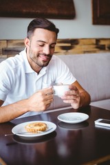 Fototapeta na wymiar Young man drinking cup of coffee and pastry beside
