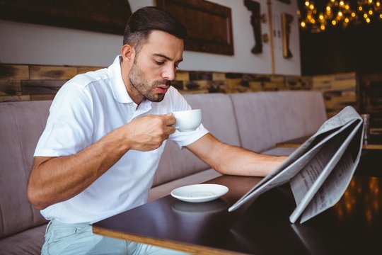 Young man drinking cup of coffee reading newspaper