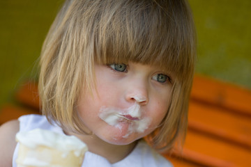 Little girl eating ice cream in a white cup in the park. It's a little soiled.