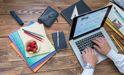 Journalist working on his new article.
Overhead view of man typing on keyboard laptop located vintage natural wooden desk with many items in creative messy disorder
