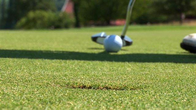 Close-up of golfer using putter to sink short putt into hole,
