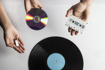 Mani che mostrano un disco in vinile, una musicassetta una cd e una chiave usb
