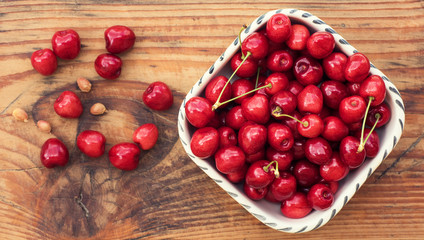 Ripe organic homegrown cherries and stones in a vintage ceramic bowl, on wooden background