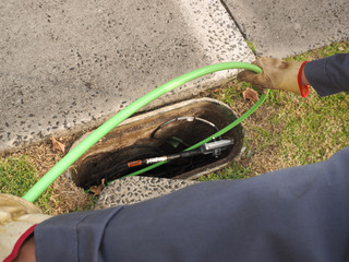 Installation of  a green fiber optic ribbon cable in a duct through a roadside communications pit,...