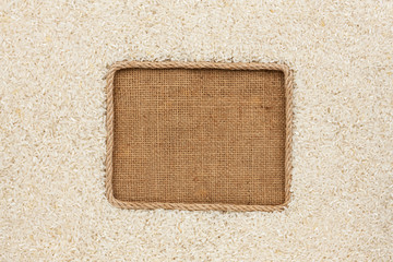Fototapeta premium Frame made of rope with rice grains on sackcloth