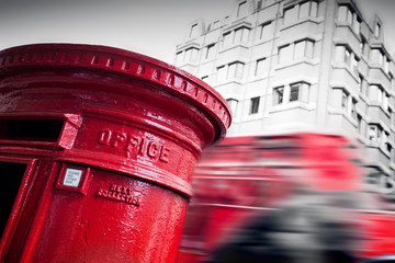 Traditional red mail letter box and red bus in motion in London, the UK.