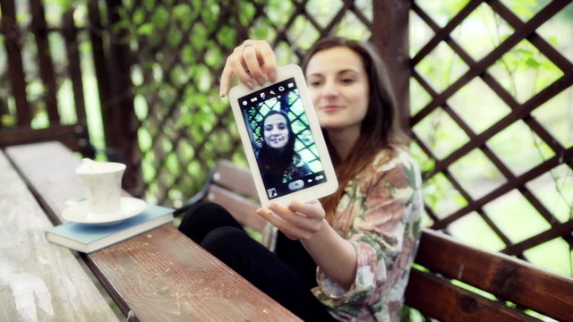 Woman sitting in the arbour and doing selfie on tablet
