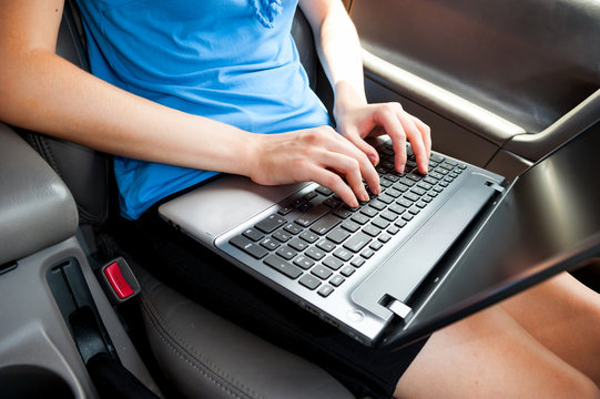 Unrecognizable businesswoman sitting in car with laptop computer on her knees. color image in horizontal orientation