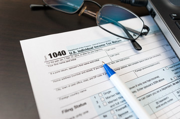 Filling Individual tax return form 1040 on a table with glasses, pen and laptop