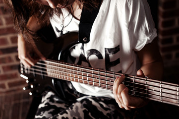Fototapeta premium Young adult girl playing five string bass guitar. Color image