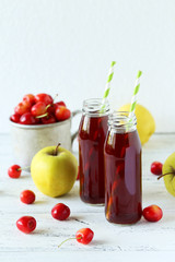 Glass of cherry juice with apple on white wooden background