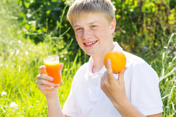 Teenager boy is holding glass with carrot juice and orange