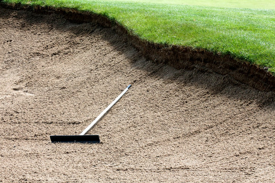 Rake In The Middle Of A Deep Sand Bunker On A Golf Course