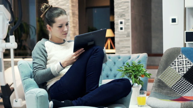 Young Woman Using Tablet Computer Sitting On Armchair At Home 
